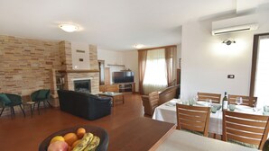 Ein Wohnzimmer mit Kamin, Fernseher, Essbereich mit Tisch und Stühlen sowie einer Obstschale.