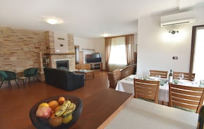 Ein Wohnzimmer mit Kamin, Fernseher, Essbereich mit Tisch und Stühlen sowie einer Obstschale.