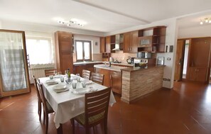 Una cocina amplia con armarios de madera, un comedor con una mesa dispuesta para cuatro personas y un ventanal que proporciona luz natural.