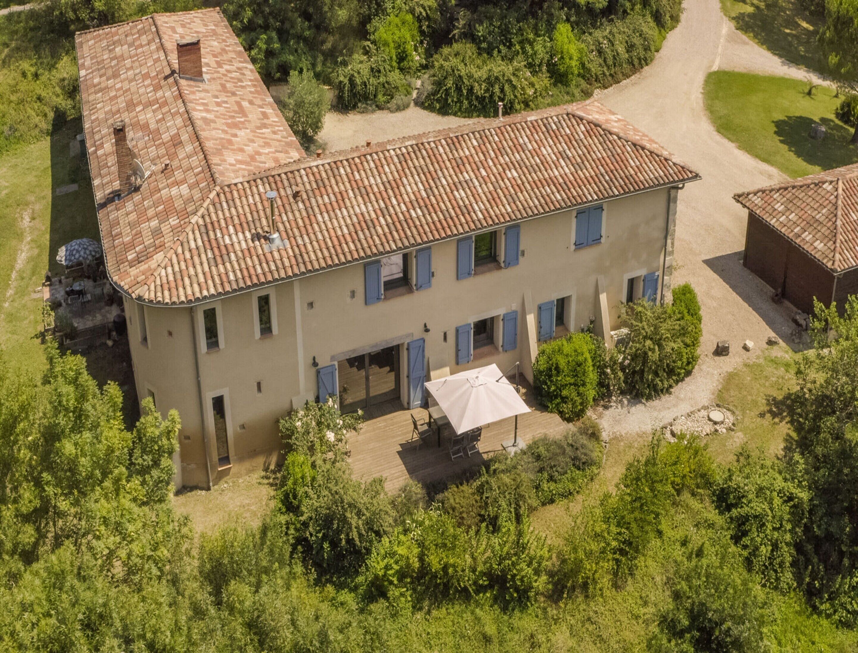 Un bâtiment à deux étages, doté d’un toit recouvert de tuiles, d’un patio abrité et entouré de verdure.
