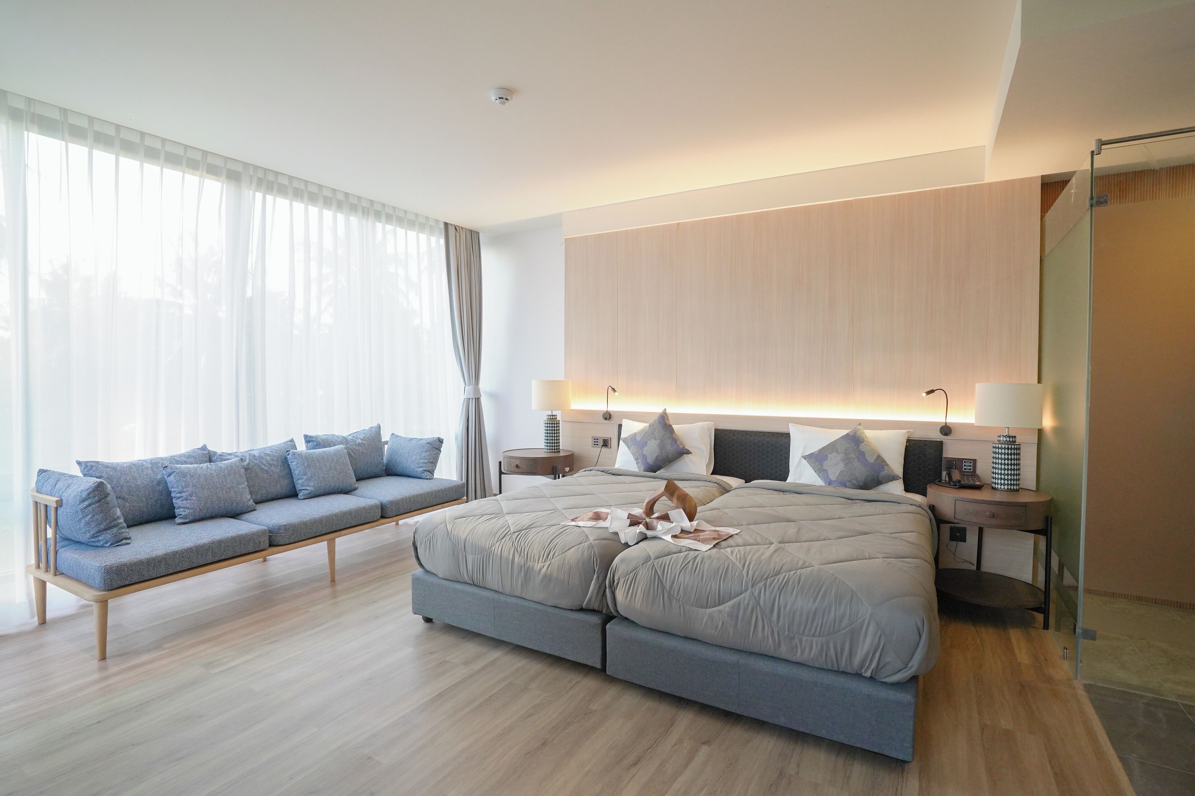 A modern bedroom with a large bed, a sofa, and a glass shower enclosure.