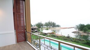 Un balcon donnant sur une piscine, une porte en bois et une vue lointaine sur une étendue d’eau avec un quai.