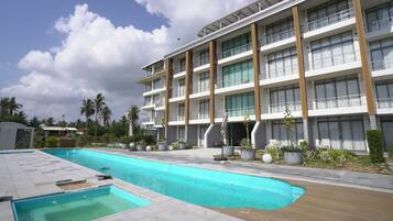 A modern hotel with a swimming pool, multiple balconies, and a landscaped garden.