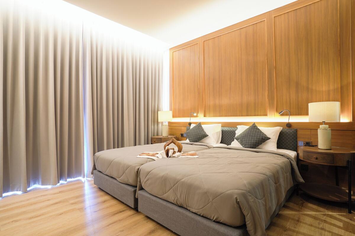 A hotel room with a large bed, wooden headboard, bedside tables, and a window with curtains.