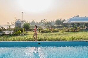 A swimming pool with a person standing at the edge, surrounded by greenery and a building in the background. - Koh Talu On Shore Resort by Koko (Bang Saphan)
