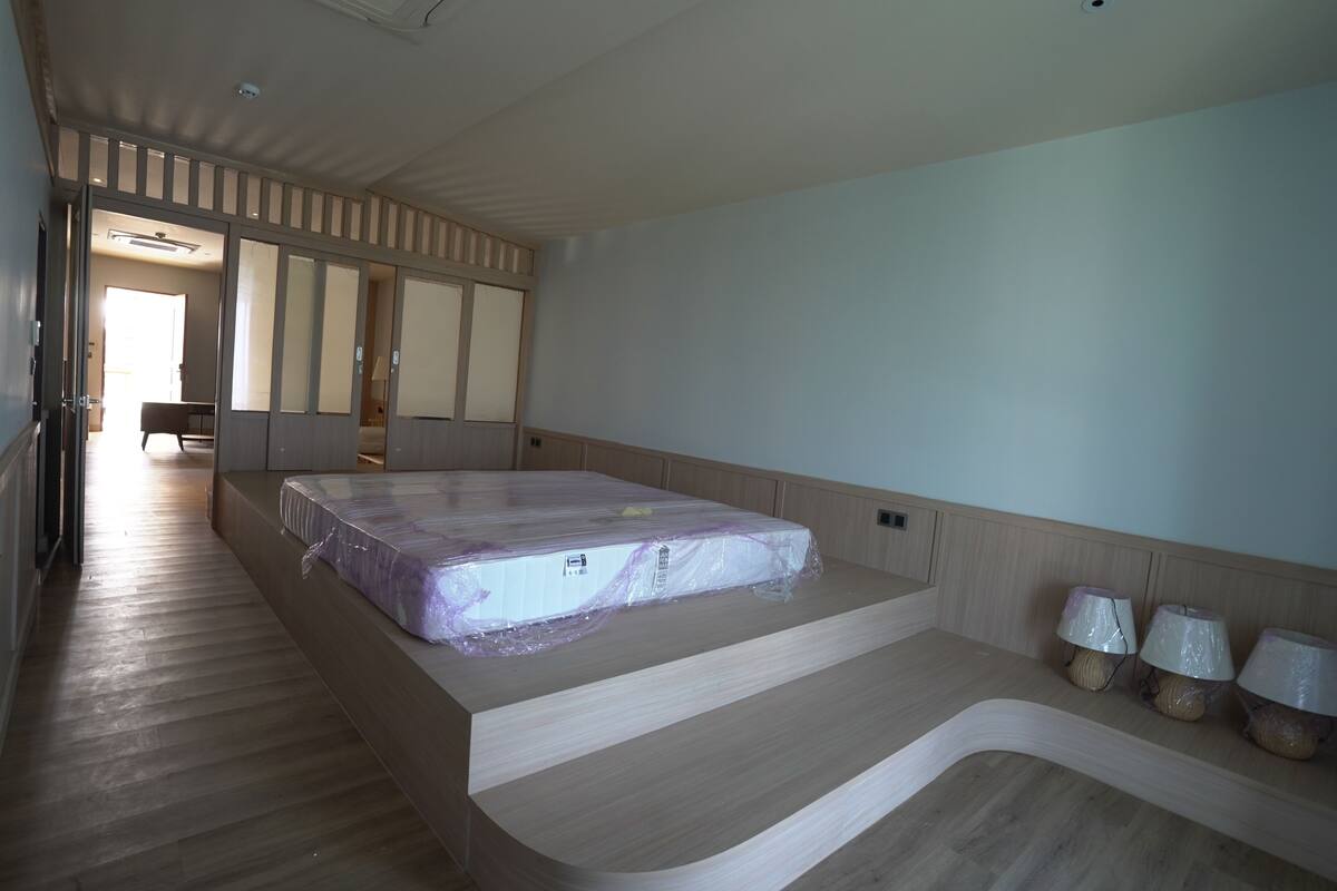 A bedroom with a large bed, a wooden floor, a built-in bench, and a view of the hallway.