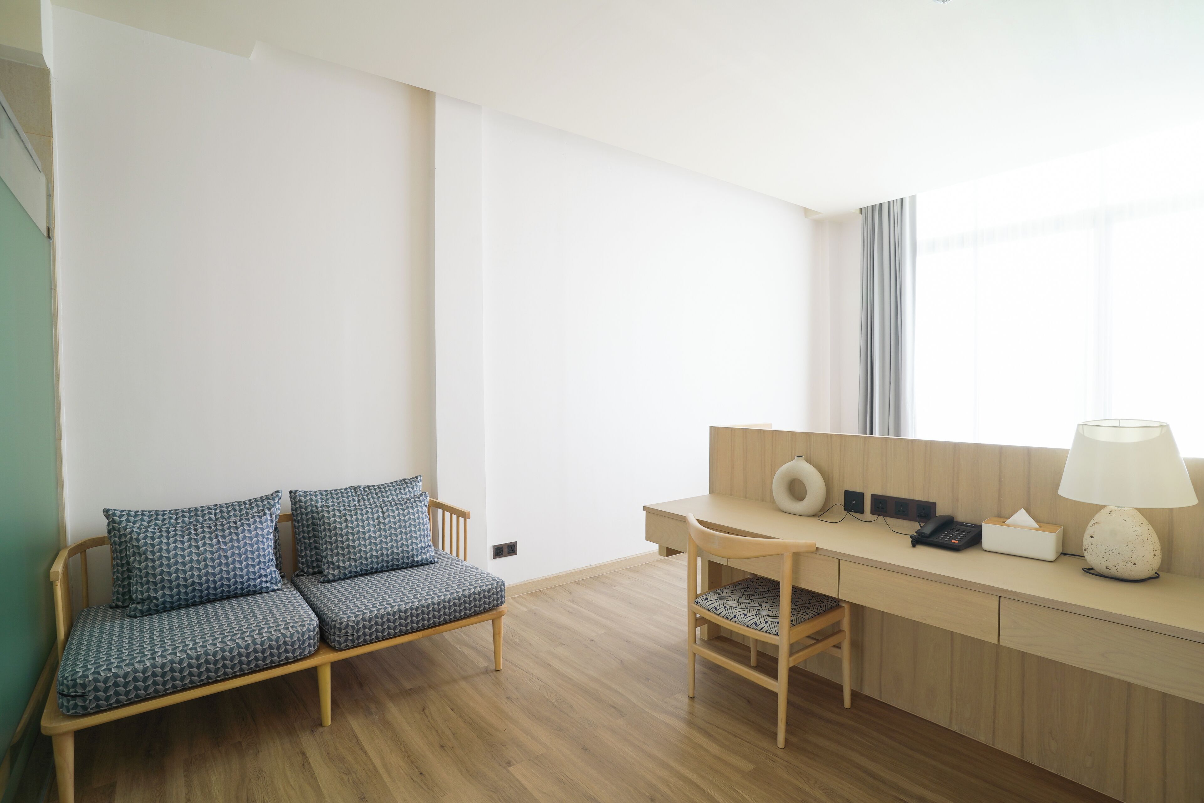 Een kamer met een houten bank, een bureau met een lamp en een stoel.