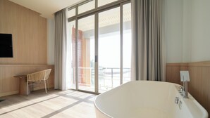 Une salle de bain moderne avec une baignoire sur pieds, une chaise en bois et une grande porte-fenêtre coulissante donnant sur un balcon.