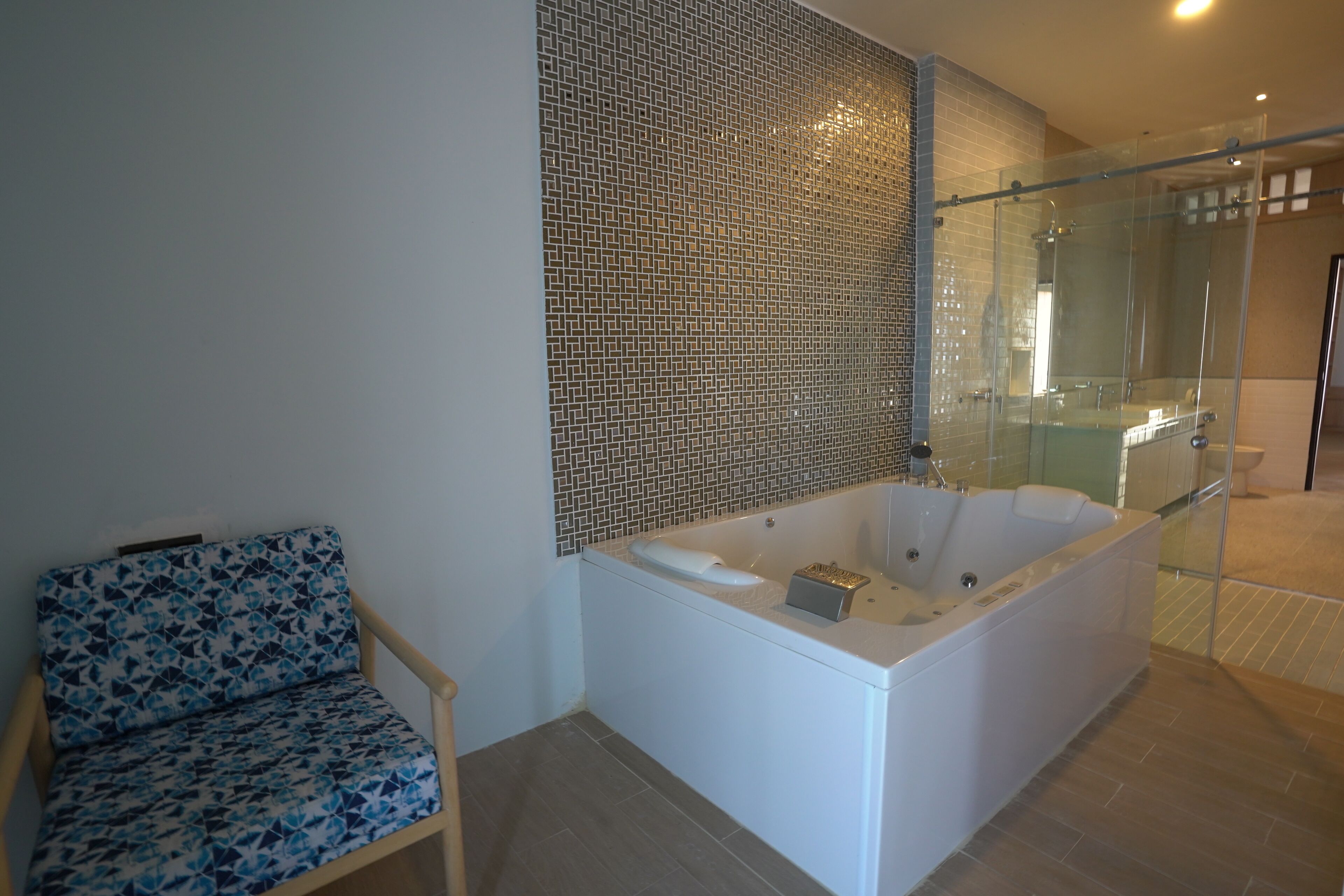 Un baño moderno con ducha de vidrio, una bañera grande y una silla estampada.