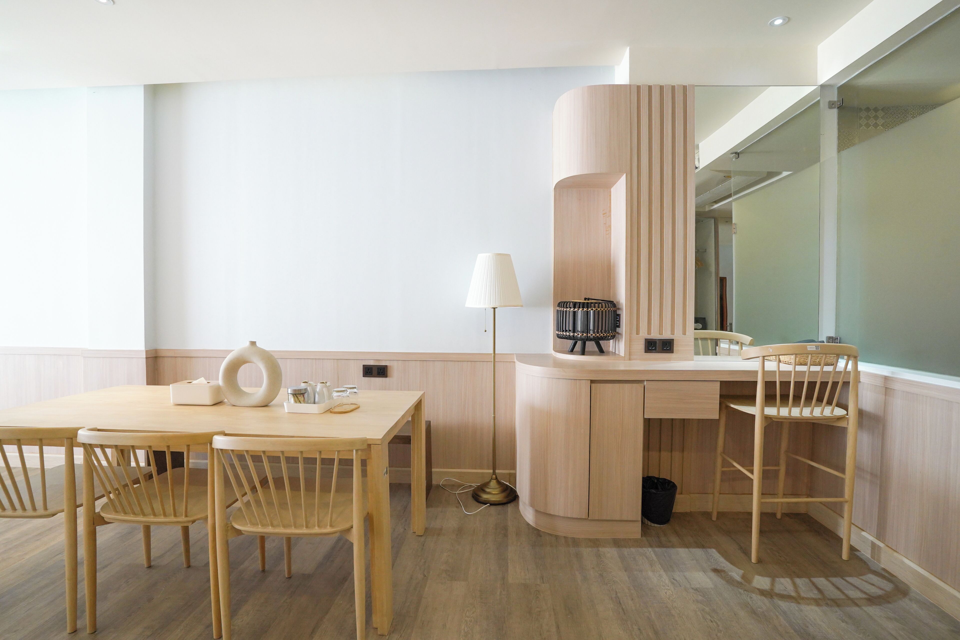 A modern room with a wooden desk, two chairs, a lamp, a small table, and a trash bin.