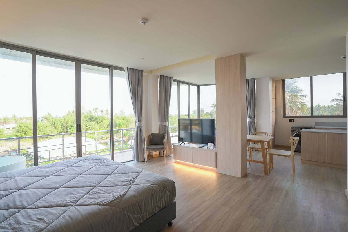 Moderni hotellihuone, jossa on suuri sänky, televisio, työpöytä tuolilla sekä parveke, jolta on näkymä vehreään maisemaan.