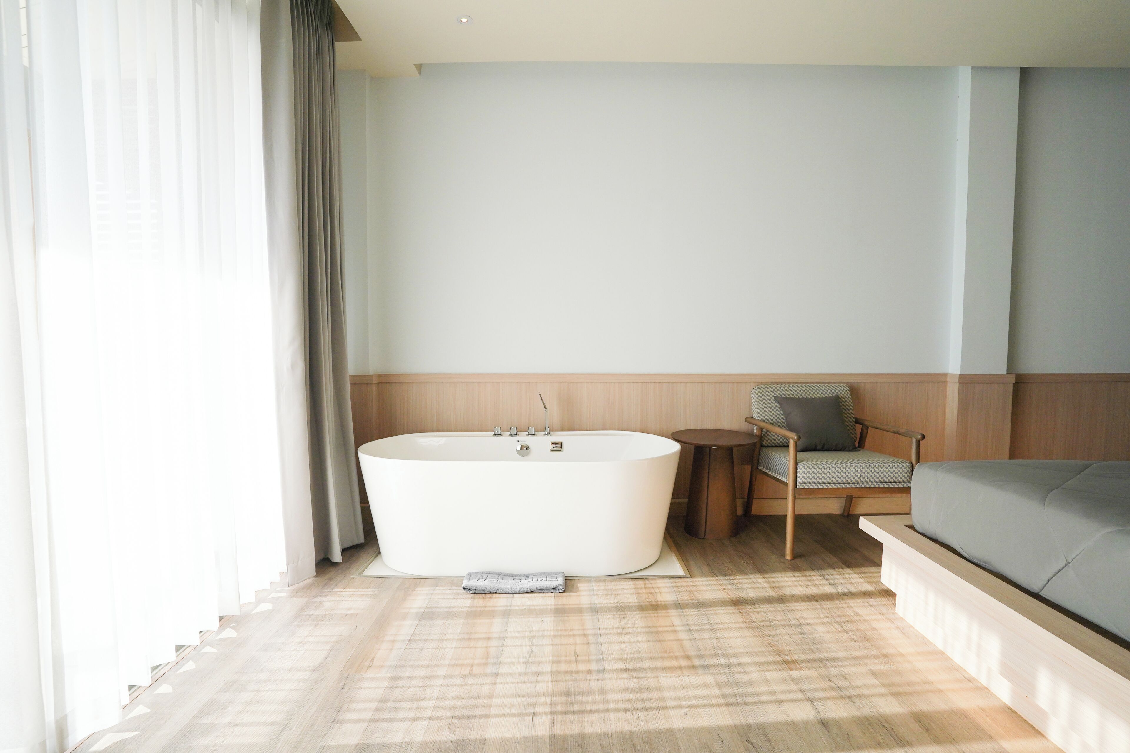 A modern bathroom with a freestanding bathtub, a small round table, a cushioned chair, and a sofa.