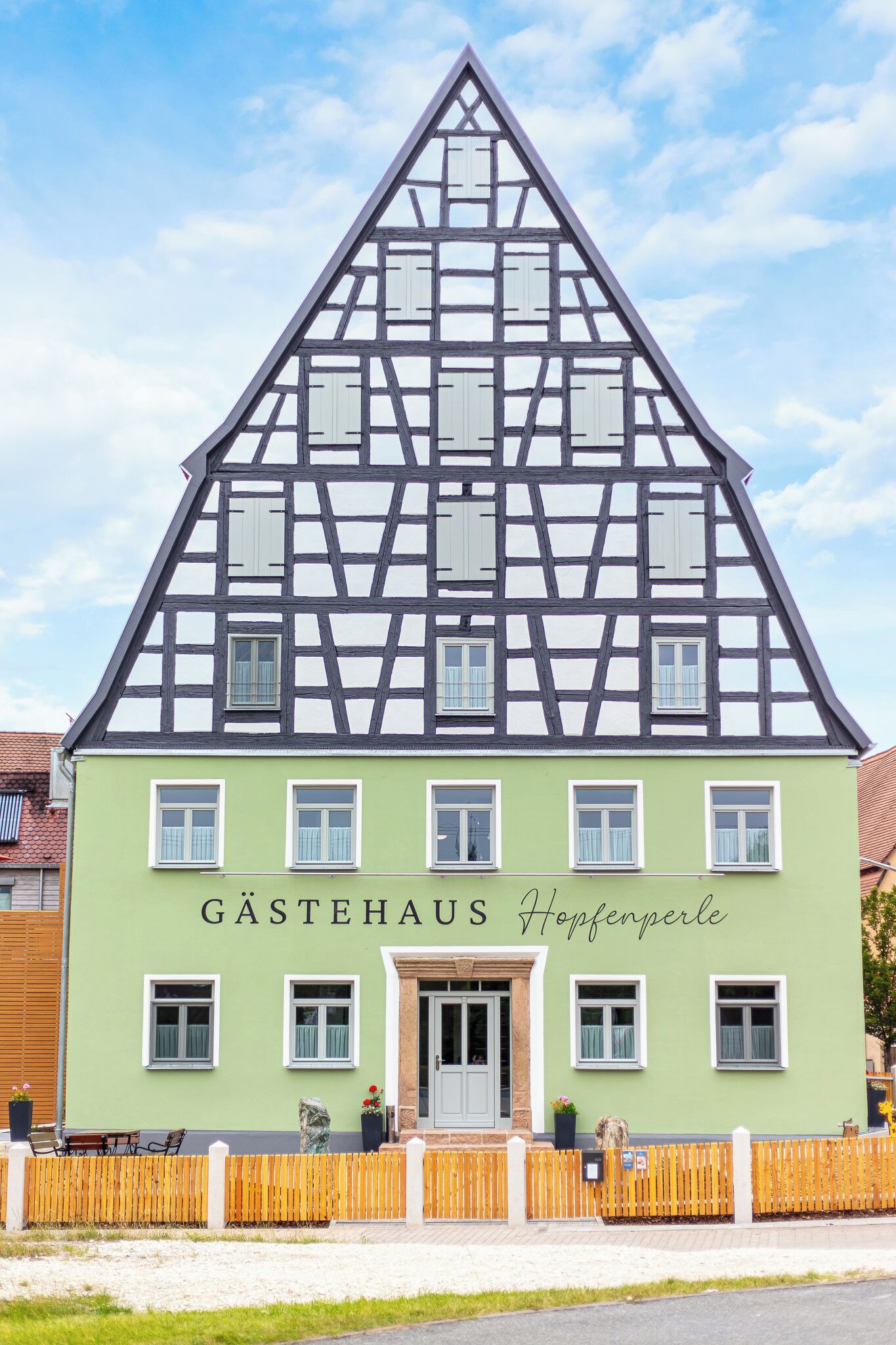 Een traditioneel vakwerkhuis met een groene gevel en een bord waarop 'GASTEHAUS Hopfenperle' staat.