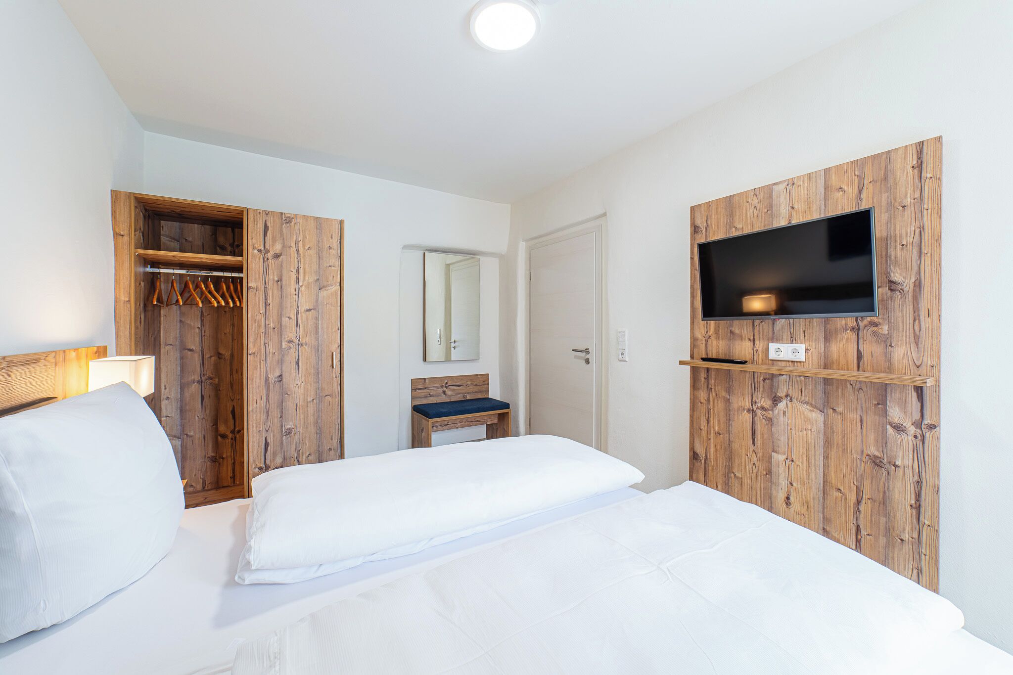Une chambre d’hôtel comprenant un lit, une armoire en bois, un miroir, un téléviseur fixé sur un panneau en bois et une petite table.