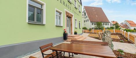 A building with a green facade, a wooden bench, and a paved patio area.