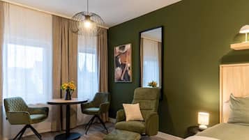 Ein Hotelzimmer mit einem Bett, einem runden Tisch mit Stühlen, einem Sofa, einem kleinen Beistelltisch mit Lampe und einem großen Spiegel an der Wand.
