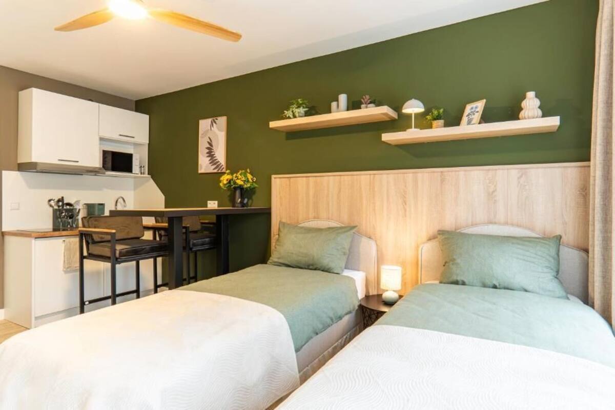 Un dormitorio con dos camas, un cabecero de madera, un escritorio pequeño con una silla, un microondas y una pared verde con estantes.