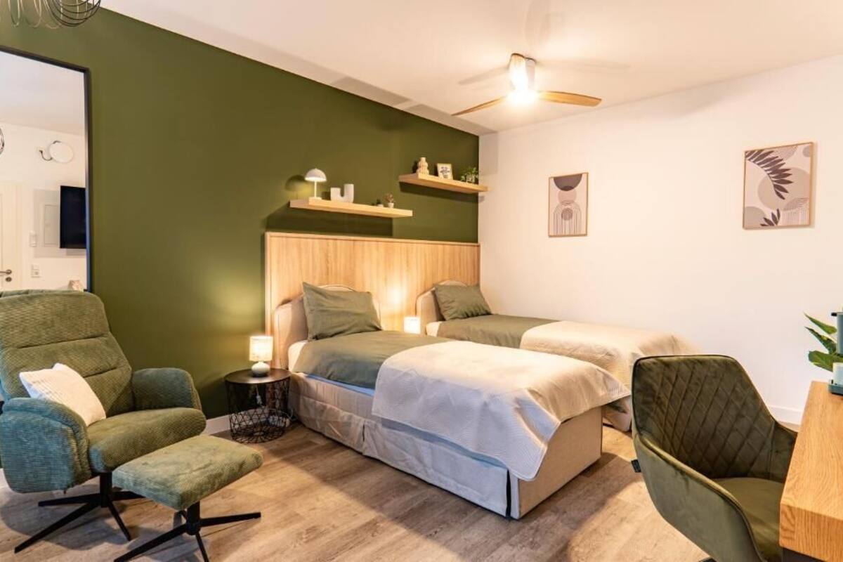 Una habitación con cama, dos sillas, escritorio, estanterías y ventilador de techo.