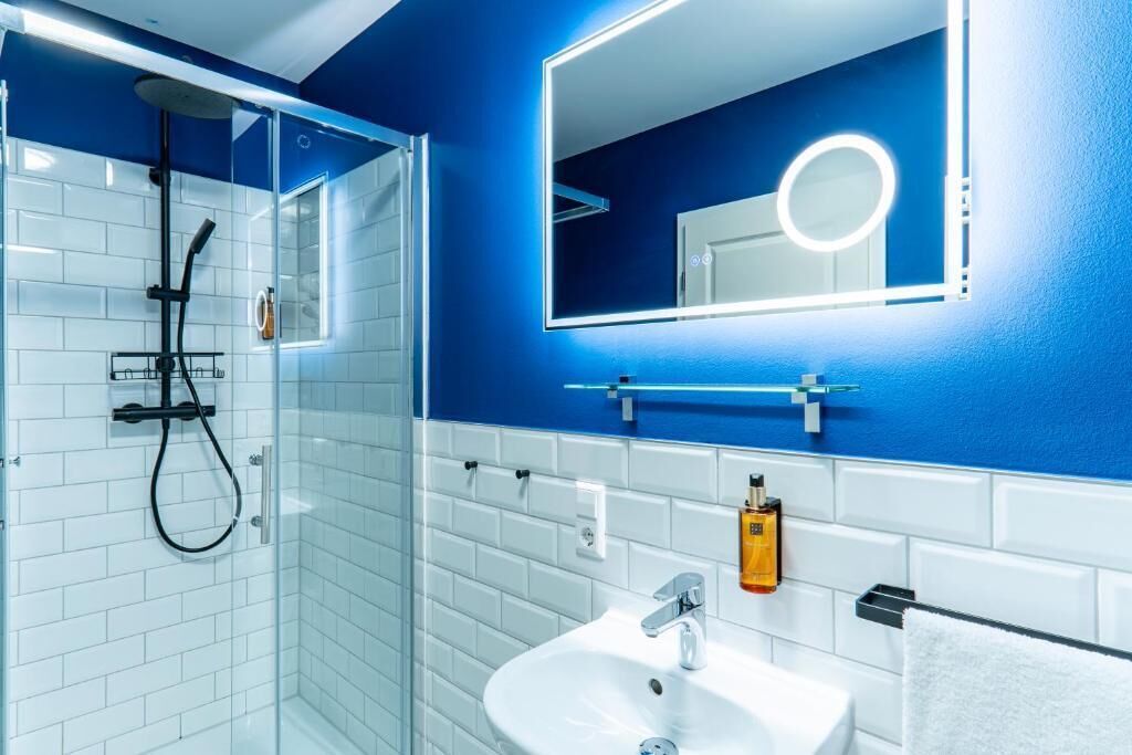 Une salle de bain moderne avec une douche à parois de verre, un lavabo blanc et un miroir doté d’un cadre éclairé.
