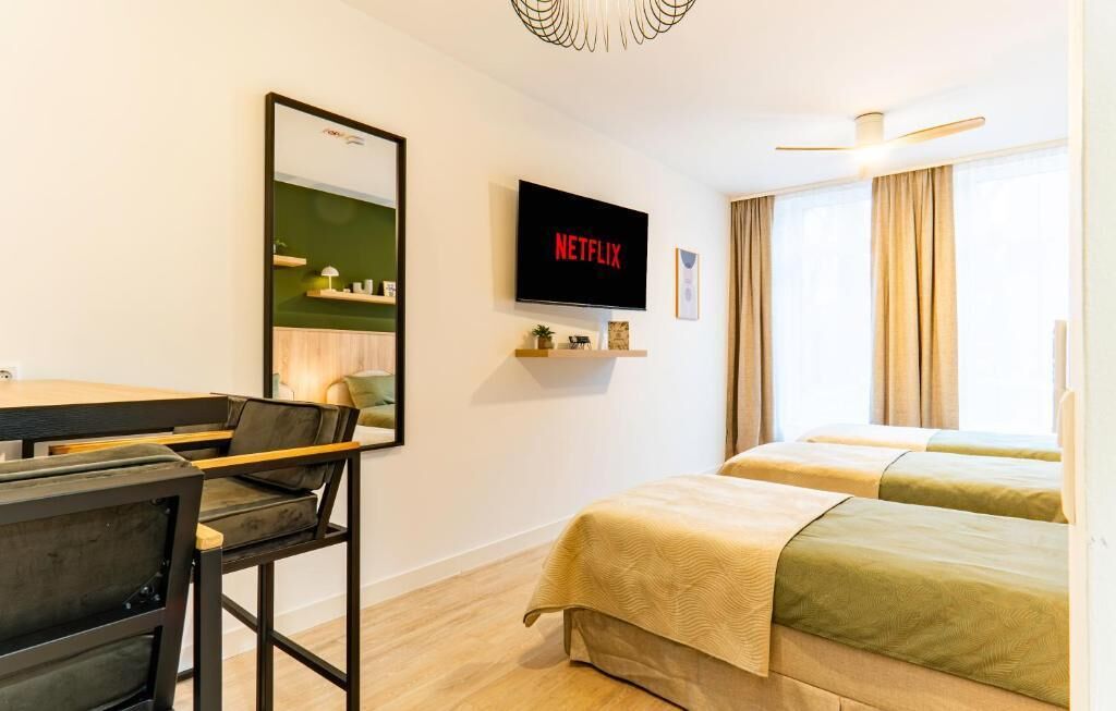 Une chambre d’hôtel comprenant un lit, un bureau avec une chaise, un téléviseur fixé au mur et une fenêtre avec des rideaux.