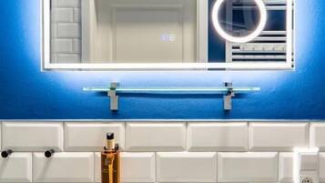 Ein Badezimmer mit einem weißen Waschbecken, einem Spiegel mit beleuchtetem Rahmen und einer blauen Wand.