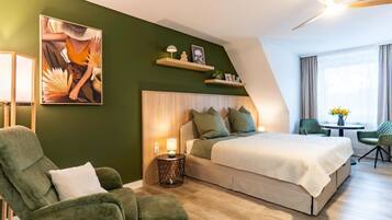 Una habitación de hotel moderna con una cama, un sillón verde, una mesita pequeña y un cuadro en la pared.