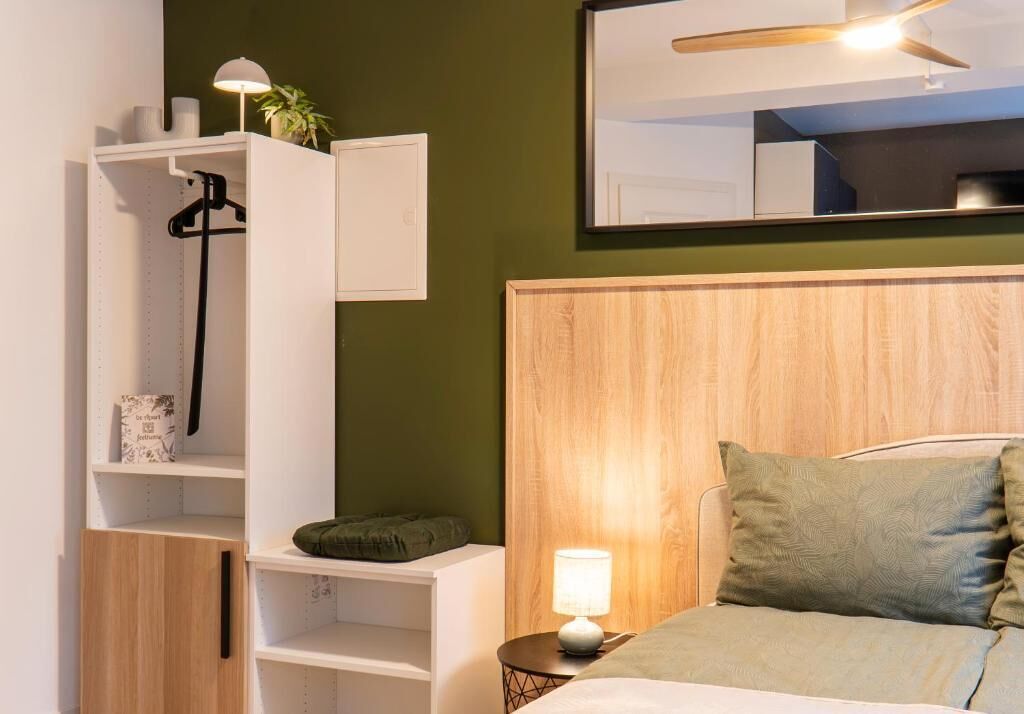 Une chambre à coucher avec un lit, une table de chevet avec une lampe, une armoire et un miroir au mur.