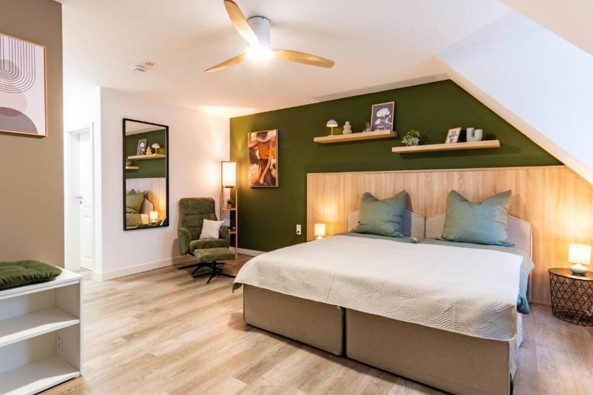 Un dormitorio con una cama, una silla, una estantería con objetos y un ventilador de techo.