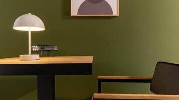 Una habitación con una pared verde, una obra de arte abstracta enmarcada, un escritorio con lámpara y una silla.