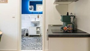 A modern kitchen with a black countertop, a stainless steel range hood, and a blue accent wall in the adjacent bathroom. - be Apart Hotel Serviced Apartments (Hannover)