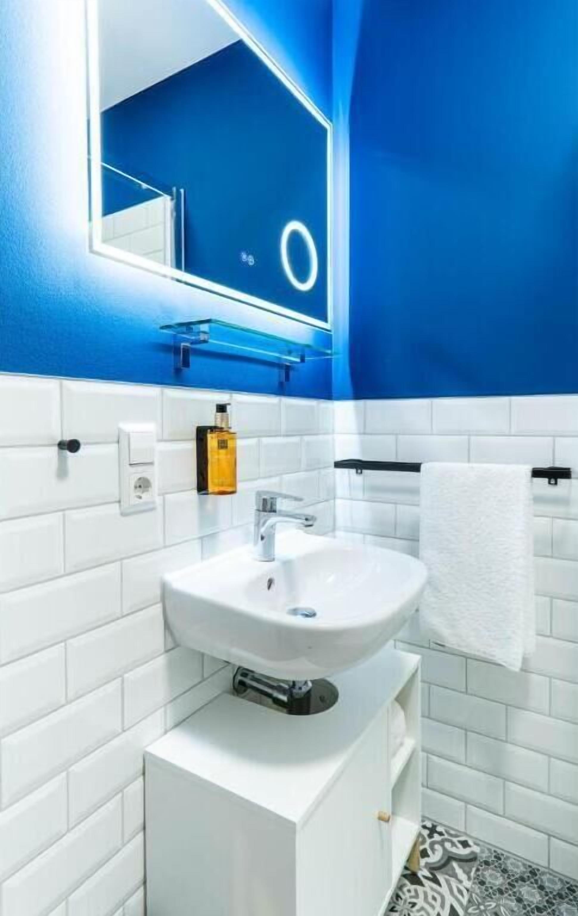 Une salle de bain avec un lavabo blanc, un miroir, un porte-serviettes et un distributeur de savon.