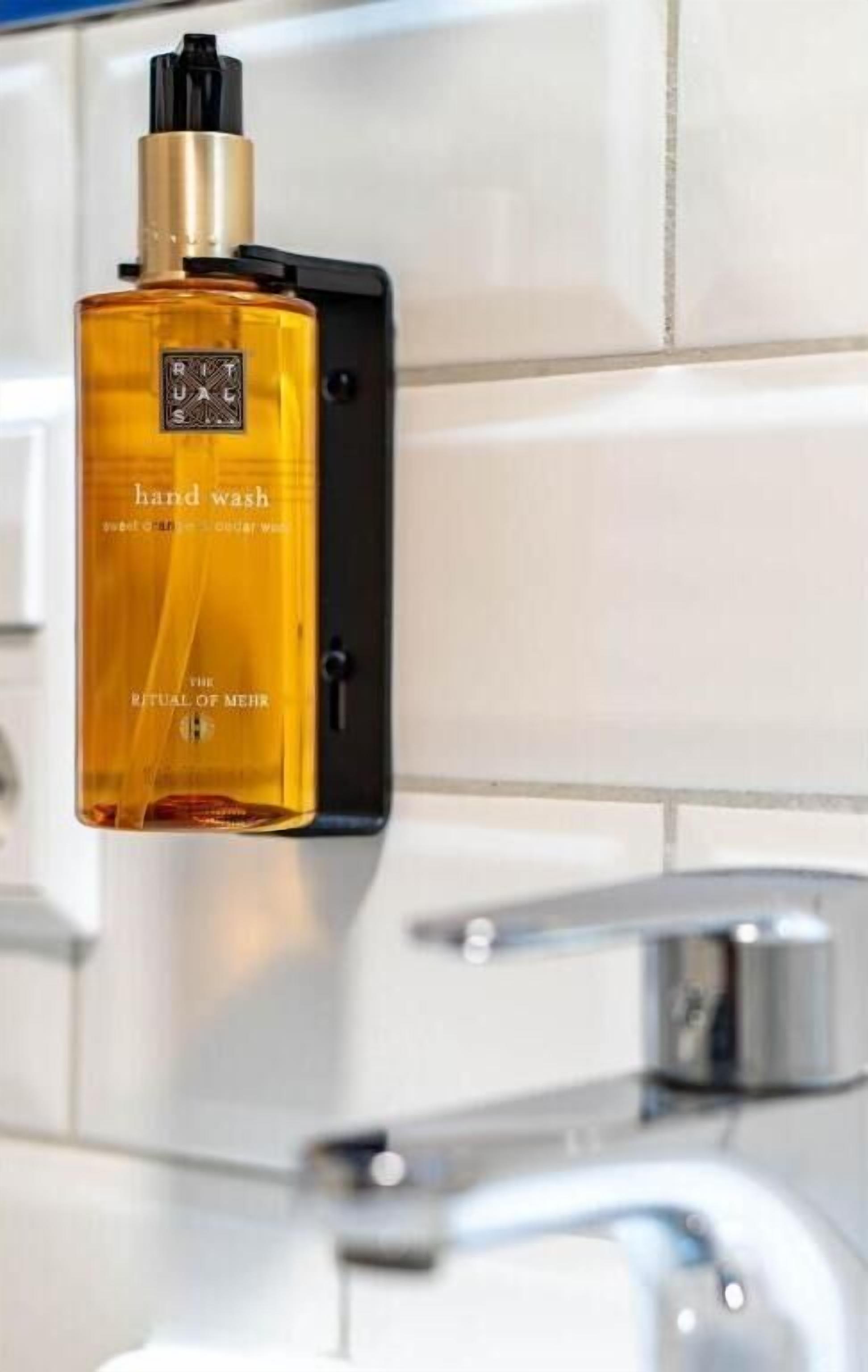 Una botella dispensadora de jabón para manos, con la etiqueta 'hand wash', en un soporte fijado a la pared.