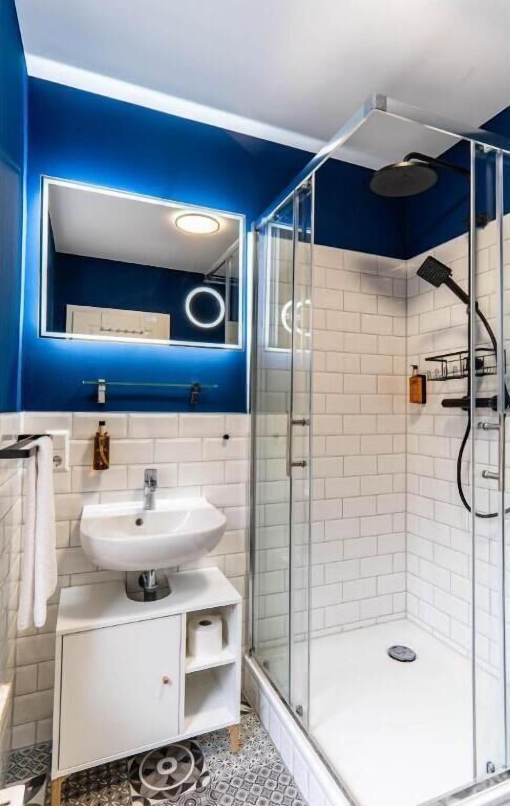A bathroom with a white sink, a mirror, a shower with a glass door, and blue walls.
