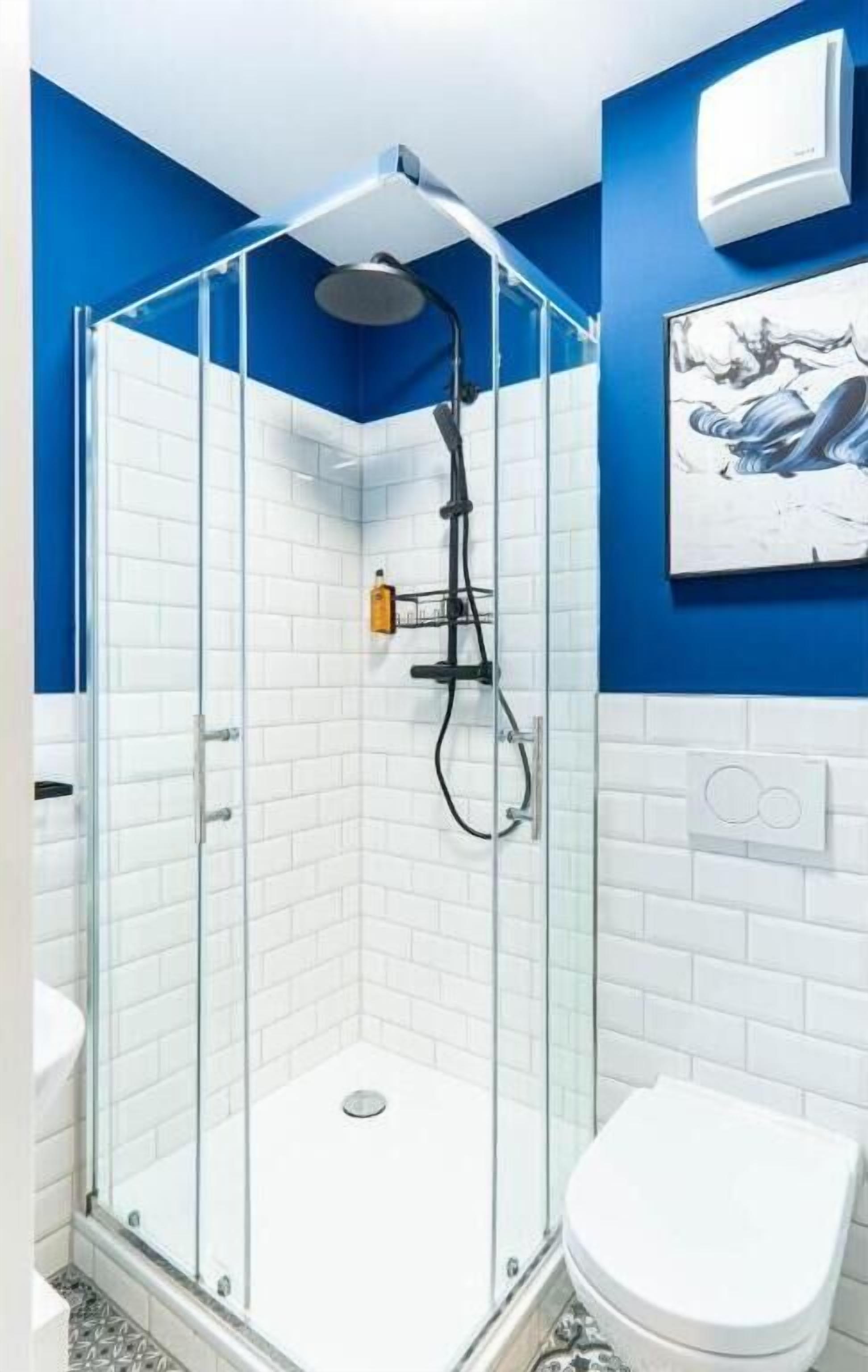 A glass-enclosed shower with a white tiled wall, a white toilet, and a blue accent wall.