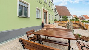 A building with a green facade, a wooden bench, and a paved patio area.