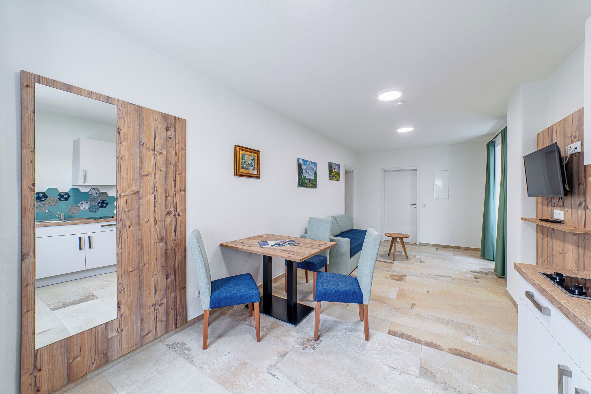 A modern kitchen with a wooden cabinet, a dining table with chairs, and a TV mounted on the wall.