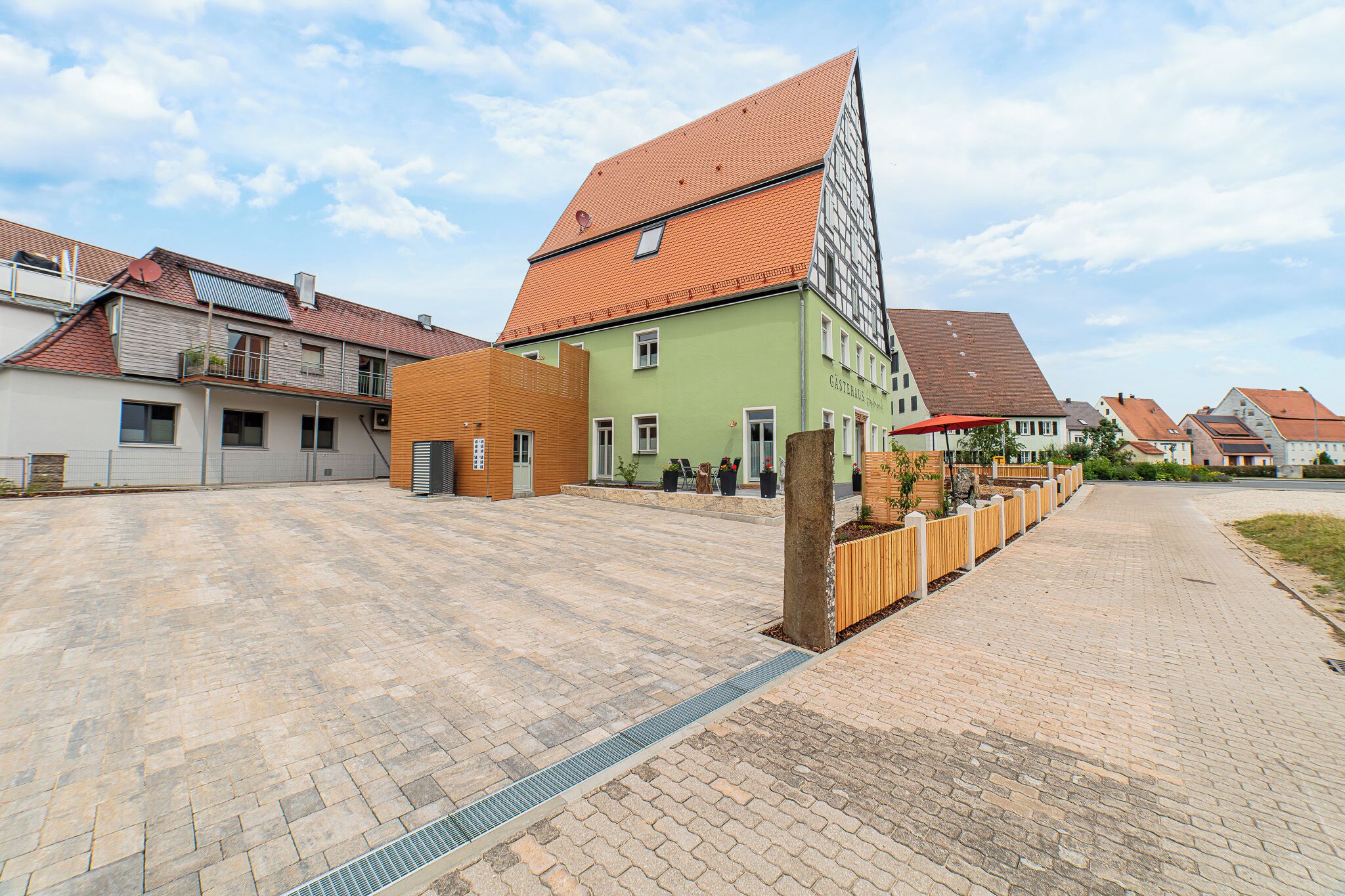 A courtyard with buildings, a wooden fence, and a paved walkway.
