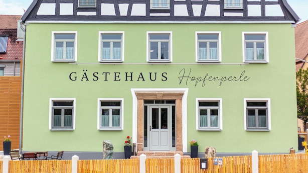 A traditional half-timbered building with a green facade and a sign reading 'GASTEHAUS Hopfenperle.'