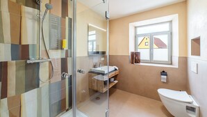 Une salle de bain avec une douche à parois de verre, des toilettes, un lavabo avec un miroir et une fenêtre donnant sur une maison.
