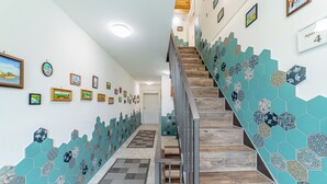 Un escalier avec des marches en bois et une rampe, menant à une porte. Les murs sont décorés de tableaux encadrés et d’un motif de carreaux.