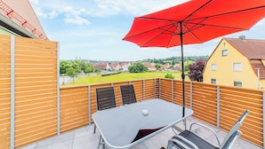 Une terrasse avec une table et des chaises, un parasol rouge et une vue sur la ville.