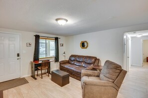 Un salon avec un canapé en cuir marron, une table basse en bois, un bureau avec une chaise et un grand miroir au mur.