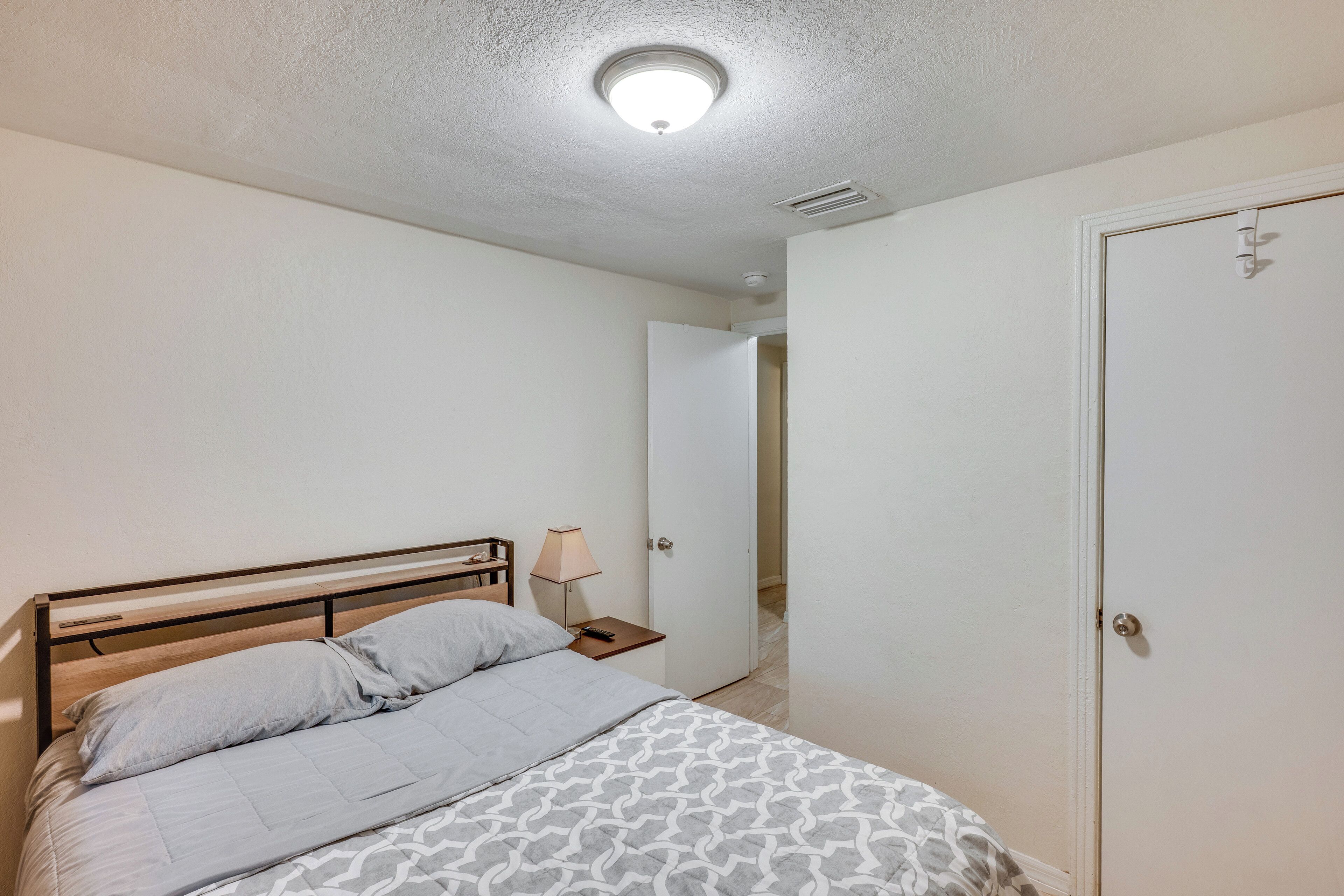 A bedroom with a bed, bedside table, lamp, and a door.