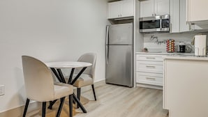 A modern kitchen with white cabinets, a stainless steel refrigerator, a microwave, and a dining area with a round table and two chairs. - 5 Mi to Dtwn Tampa + Riverwalk: Couple's Getaway (Tampa)