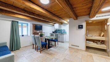 A room with a wooden ceiling, a dining area with chairs and a table, a kitchen with cabinets and a TV, and a sauna area.