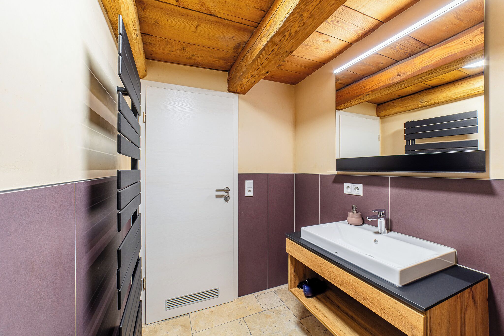 Une salle de bain avec un plafond en bois, une porte blanche, un lavabo avec un miroir au-dessus et un porte-serviettes.