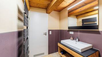 Une salle de bain avec un plafond en bois, une porte blanche, un lavabo avec un miroir au-dessus et un porte-serviettes.