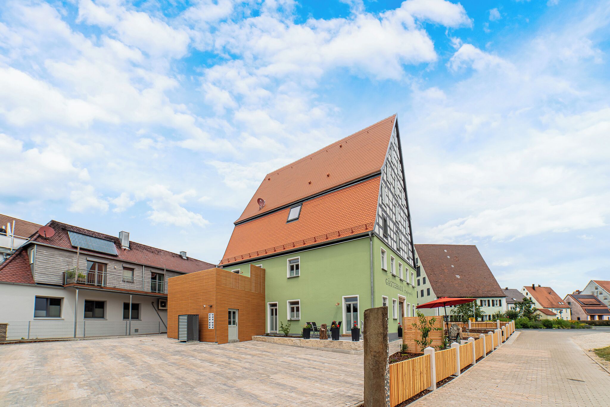 A residential building with a sloped roof, a green facade, and a paved courtyard.
