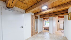 Um corredor com vigas de madeira no teto, uma porta branca e vista para um quarto com cama e radiador.