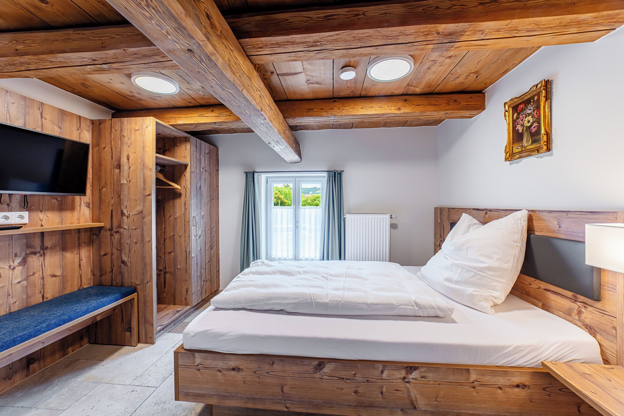 Ein Zimmer aus Holz mit einem Bett, einer Bank, einem Fernseher und einem Fenster mit Vorhängen.